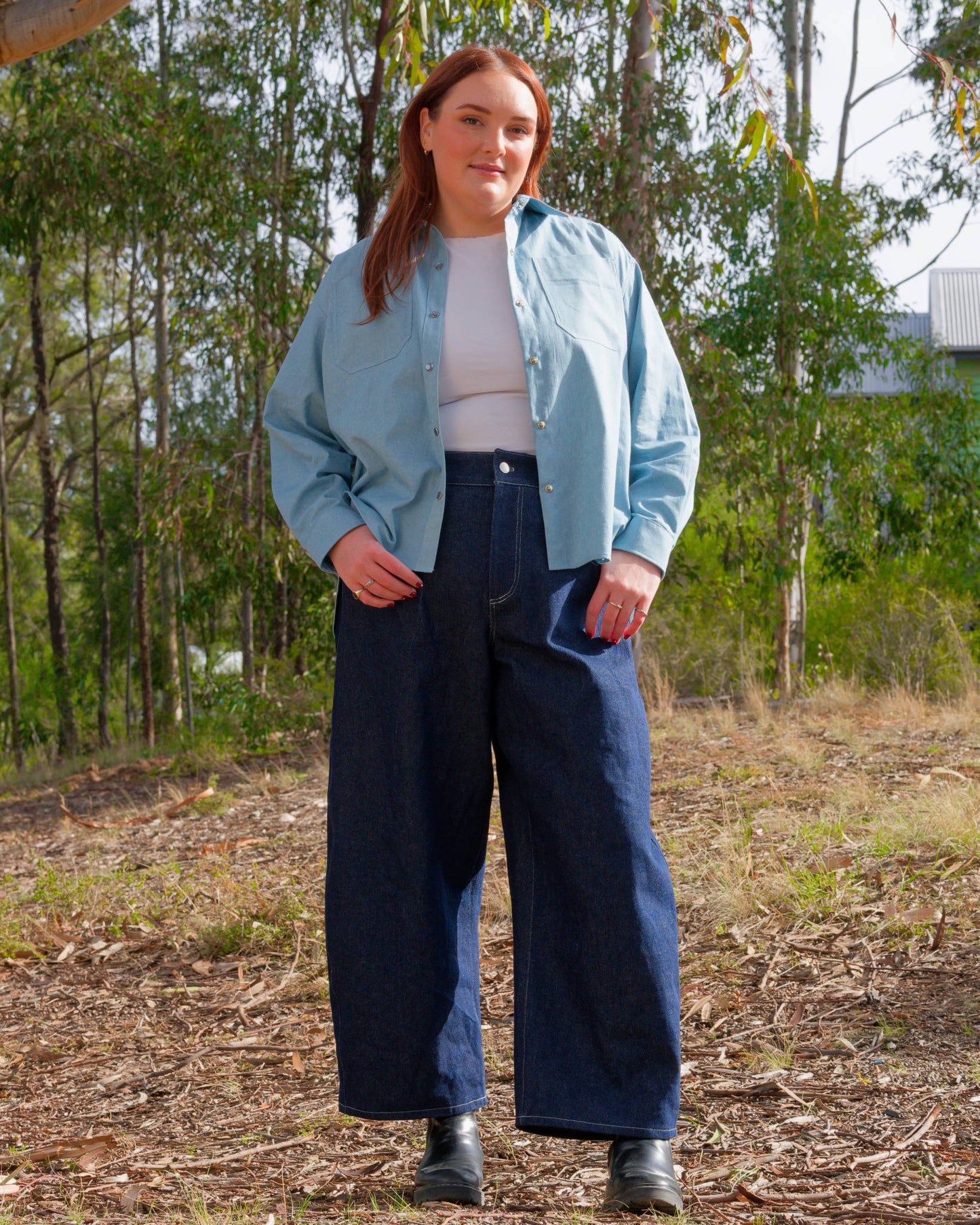 Person wearing a light blue jacket and dark blue pants standing in a natural setting with trees and grass.