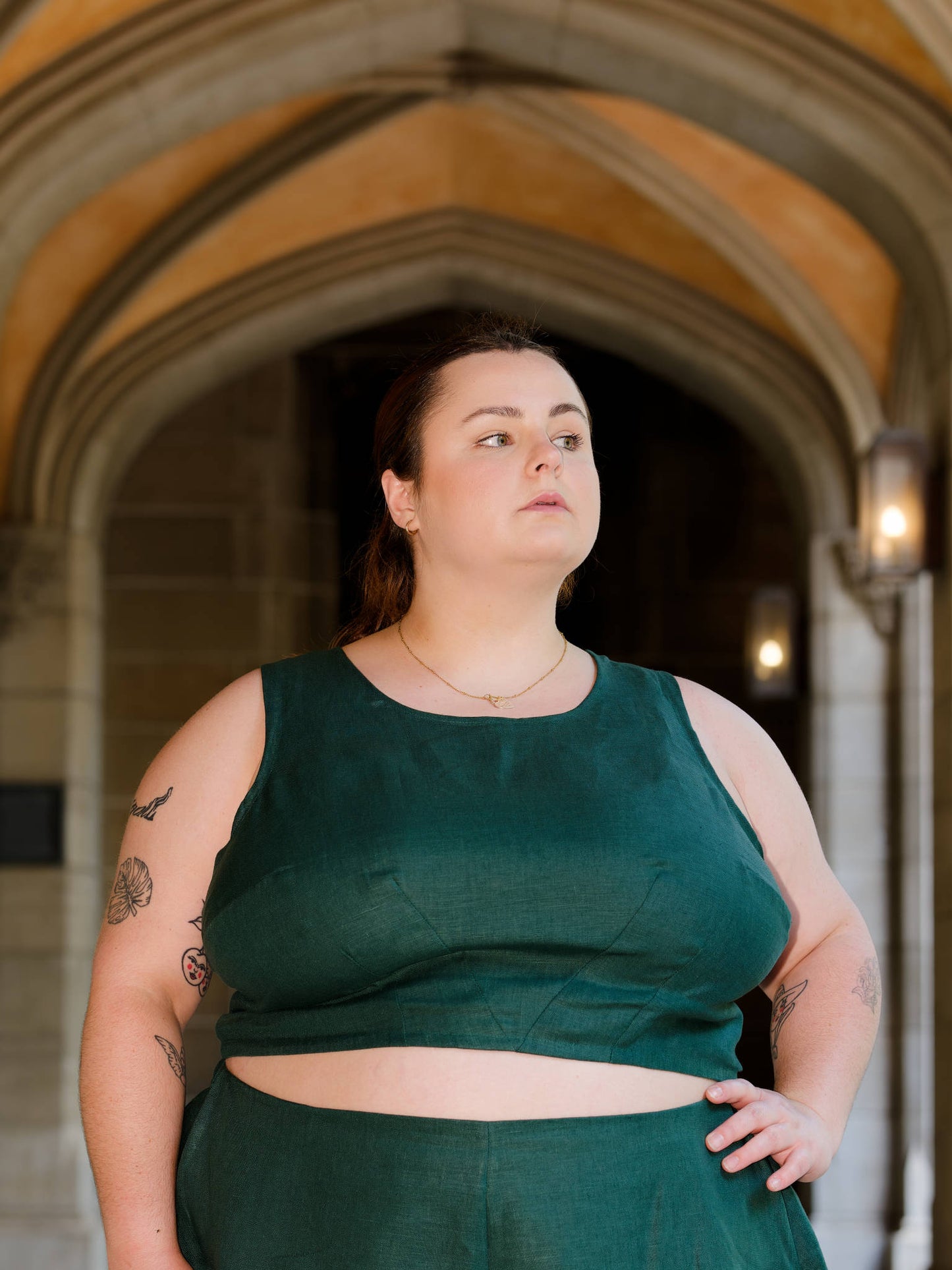 Hannah, hand on hip, modelling a green sleeveless crop top in a building with stone archways.