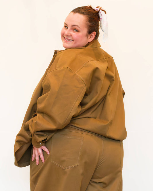 Hannah, facing backwards against a white wall, modelling khaki wide-leg jeans and a khaki chore jacket.