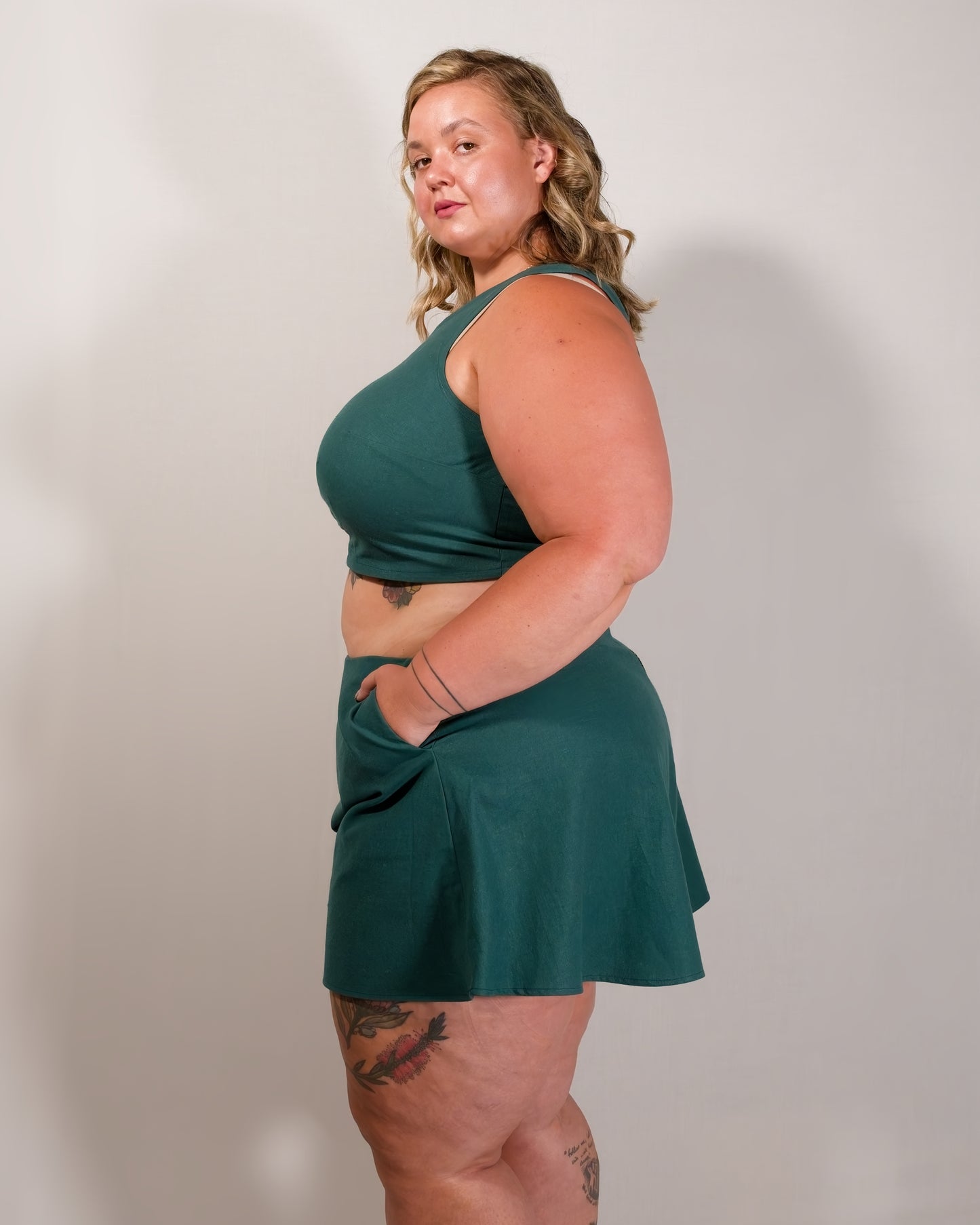 Left side of flared shorts in emerald green. Model has hand in pocket. Paired with matching sleeveless crop top.