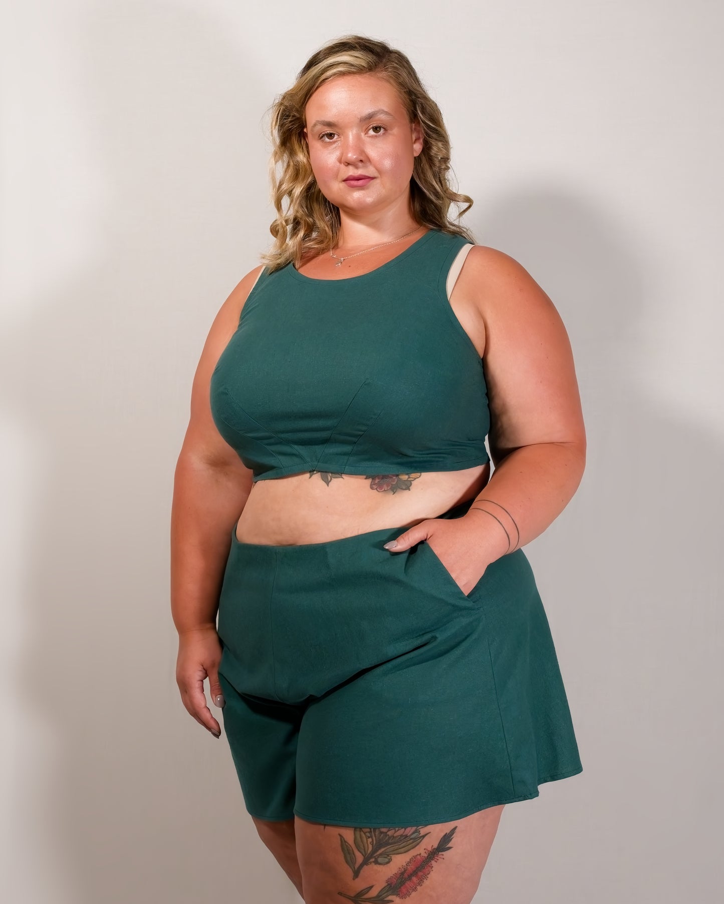 Flared shorts in emerald green. Model has hand in left pocket. Paired with matching sleeveless crop top.