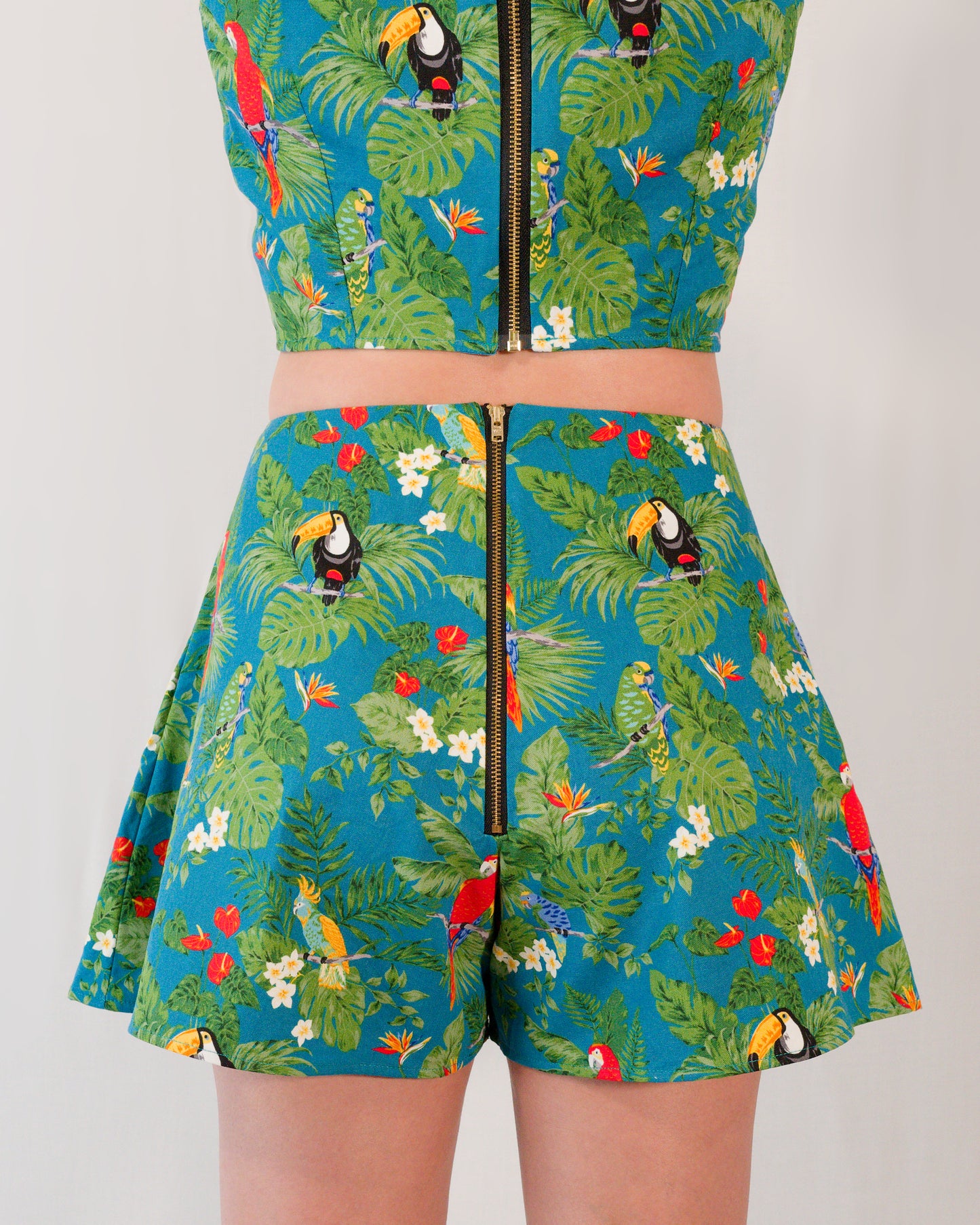 Back of flared shorts in a turquoise parrot print with a gold metal zipper closure centre-back. Zipper lines up with zipper on matching crop top.