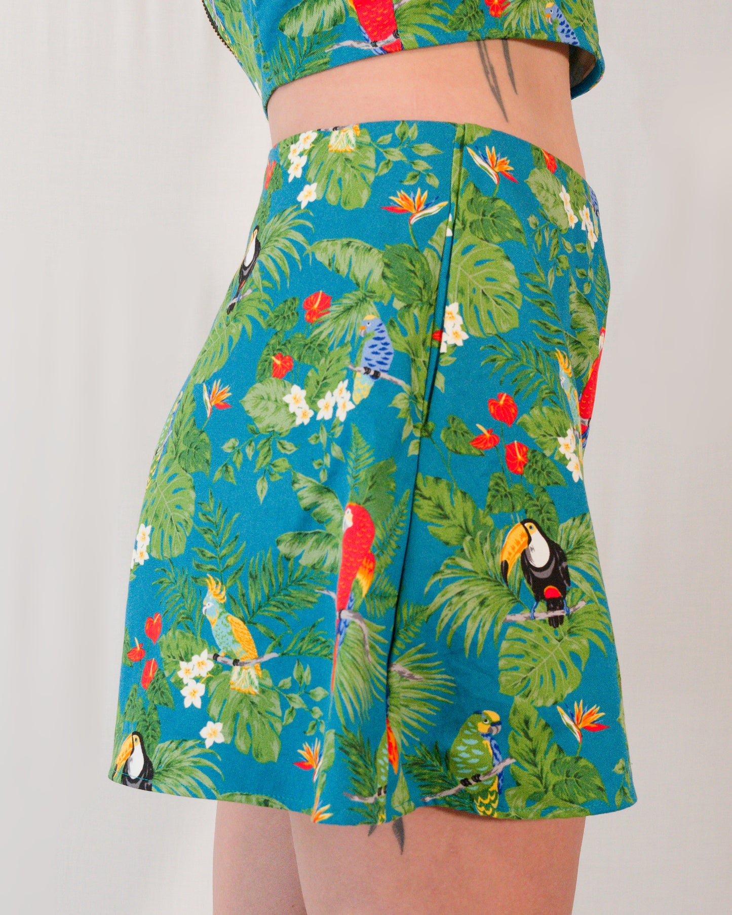 Right side of flared shorts in a turquoise print with plants, parrots and toucans. Side pocket is mostly hidden.