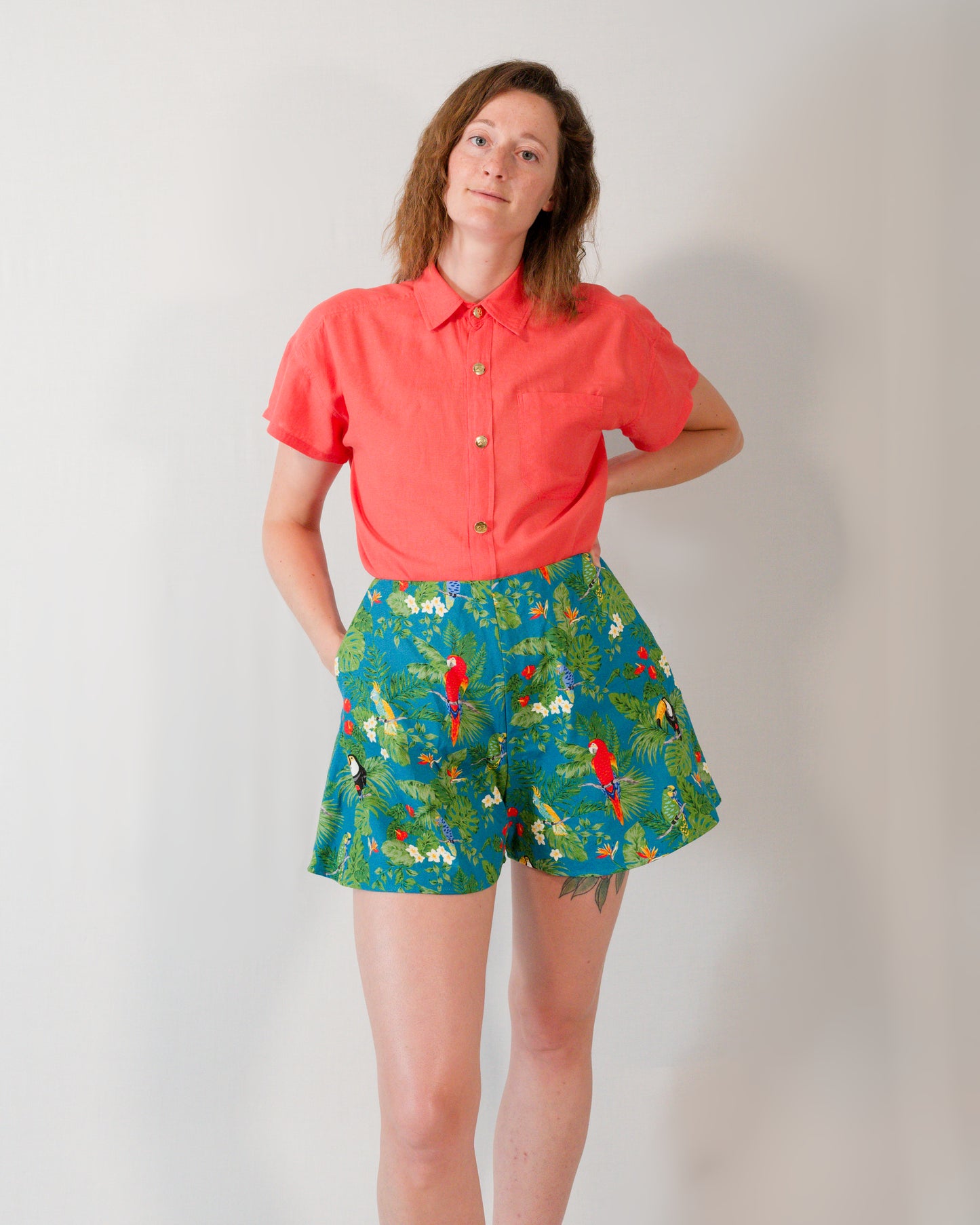 Front of flared shorts in a turquoise parrot print. Paired with a short-sleeved blouse in callistemon red, tucked in.