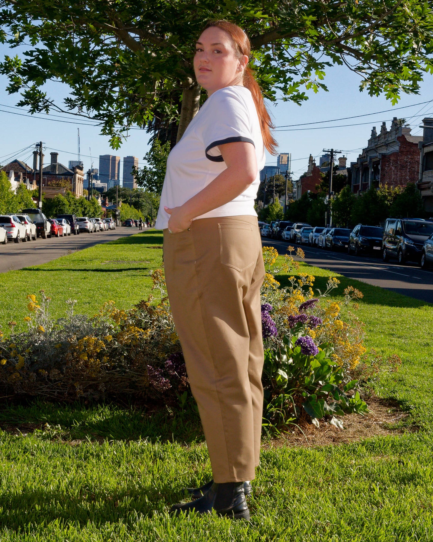 Lydia, facing side-on, modelling a white t-shirt and khaki barrel-leg jeans on a nature strip.