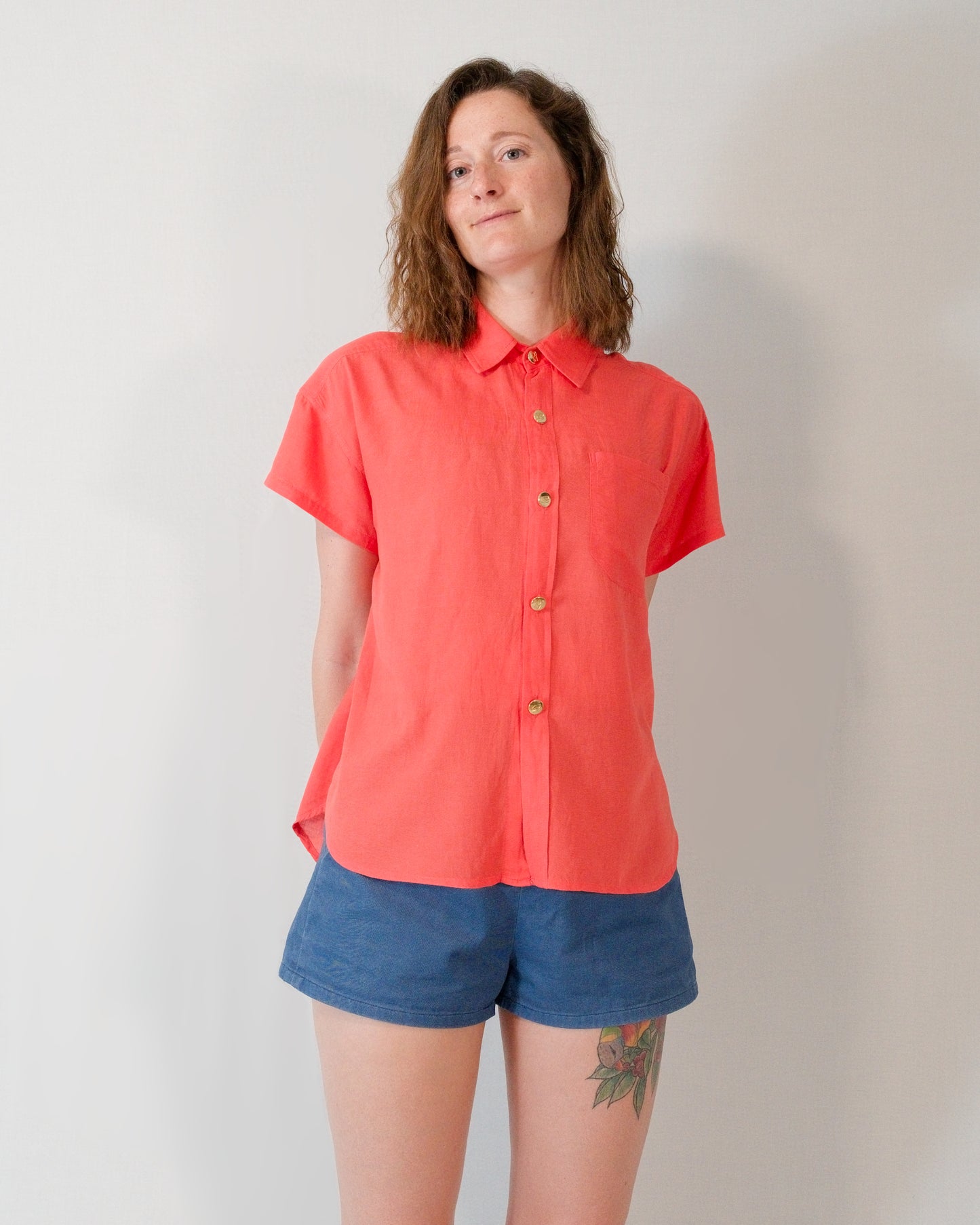 Front of a short-sleeved blouse in callistemon red with collar, brass buttons and left breast pocket.