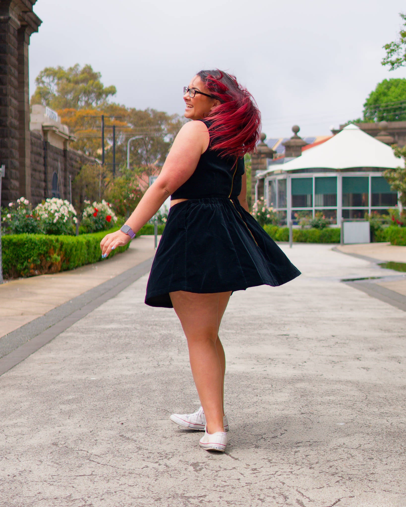 Veronica twirling in a leafy promenade, modelling a black velvet sleeveless crop top and mini skirt