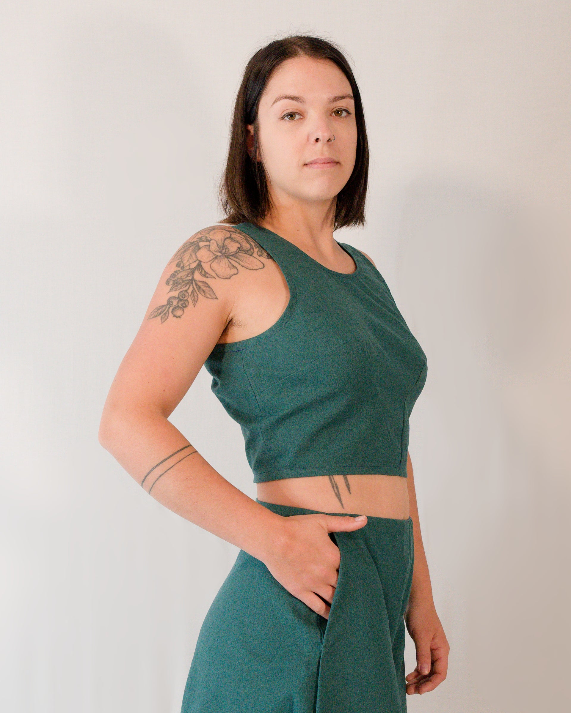 A sleeveless crop top paired with matching flared shorts, both in deep emerald. Model has one hand in right pocket.