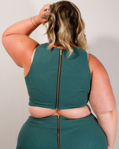 Back of a sleeveless crop top in deep emerald with a gold metal zipper centre-back.