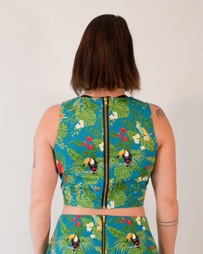 Back of a sleeveless crop top in a turquoise parrot print with a gold metal zipper centre-back.