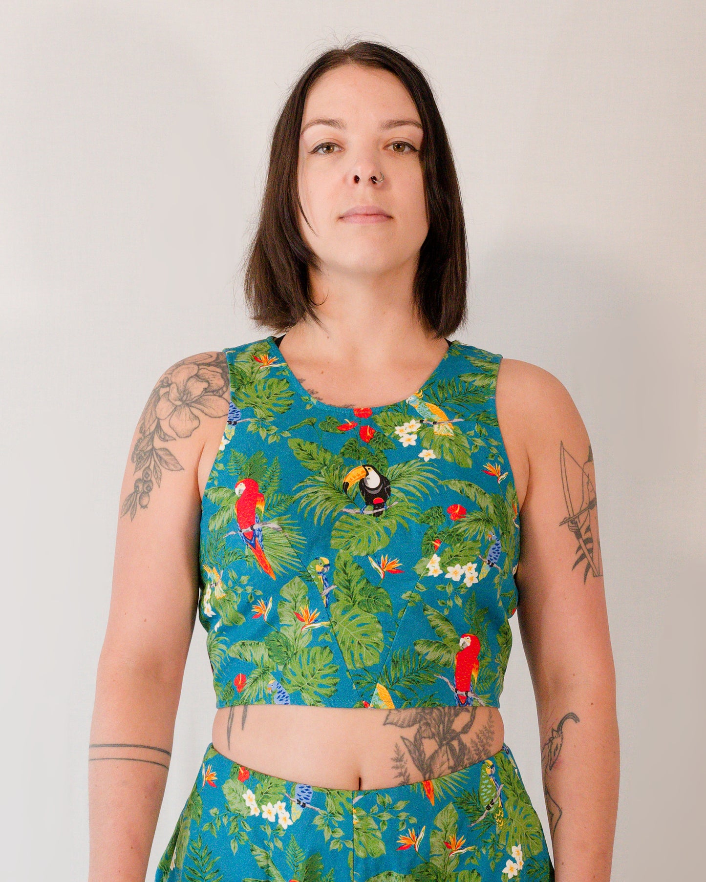 Front of a sleeveless crop top in a turquoise parrot print. The two waist darts form a V-shape below the bust.
