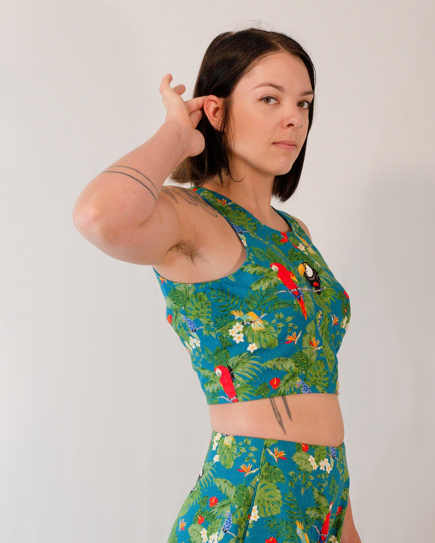Right side of a sleeveless crop top in a turquoise print with plants, parrots and toucans.