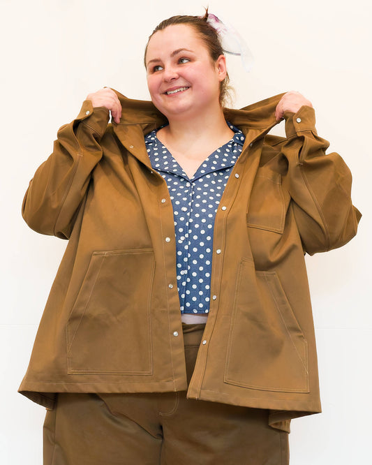 Hannah, in front of a white wall, modelling khaki wide-leg jeans and a khaki chore jacket over a a blue polkadot shirt.