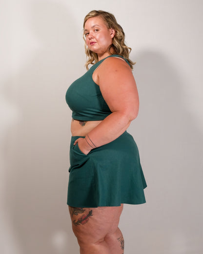 Left side of flared shorts in emerald green. Model has hand in pocket. Paired with matching sleeveless crop top.