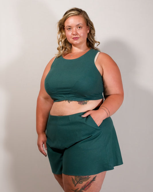 Flared shorts in emerald green. Model has hand in left pocket. Paired with matching sleeveless crop top.