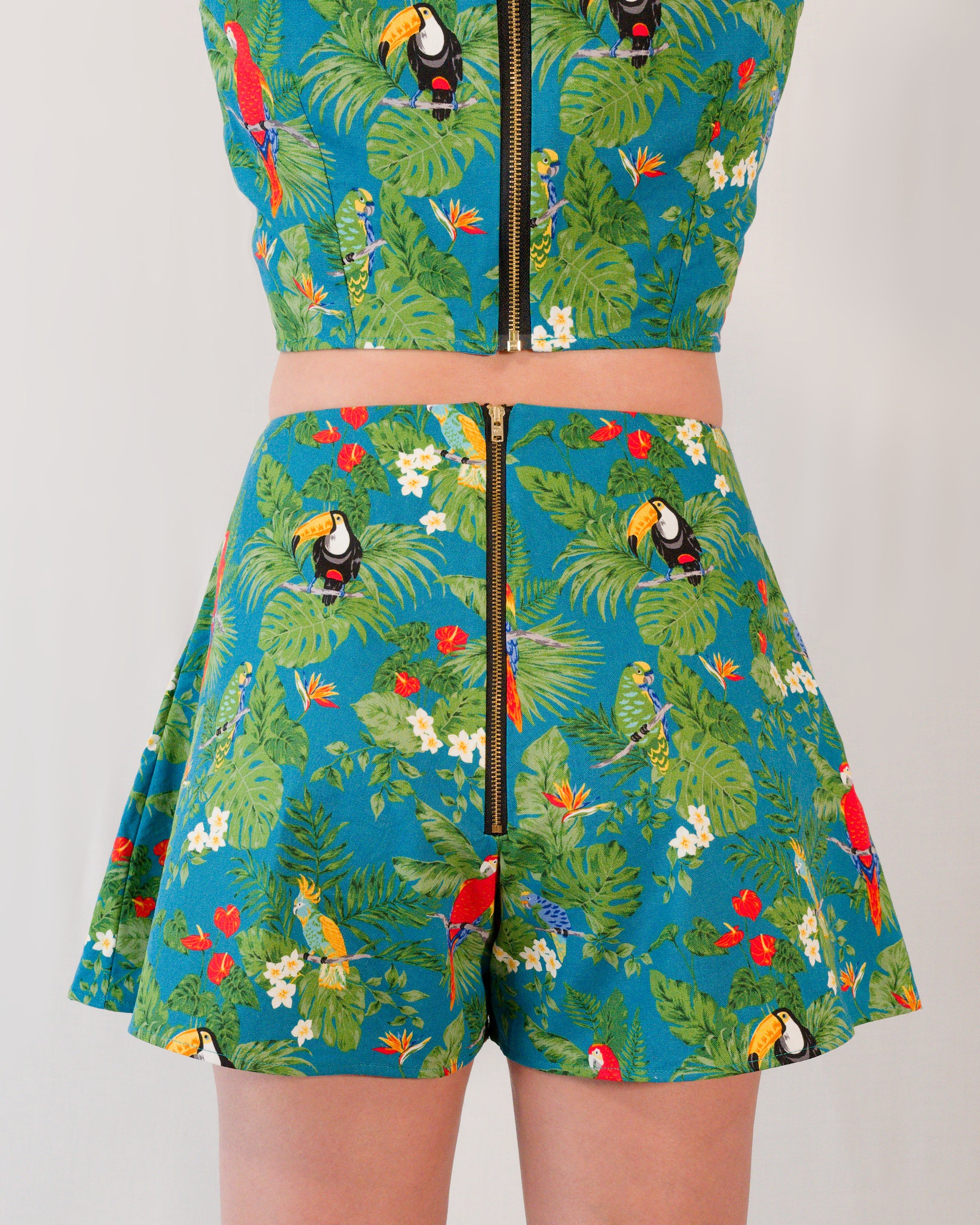 Back of flared shorts in a turquoise parrot print with a gold metal zipper closure centre-back. Zipper lines up with zipper on matching crop top.