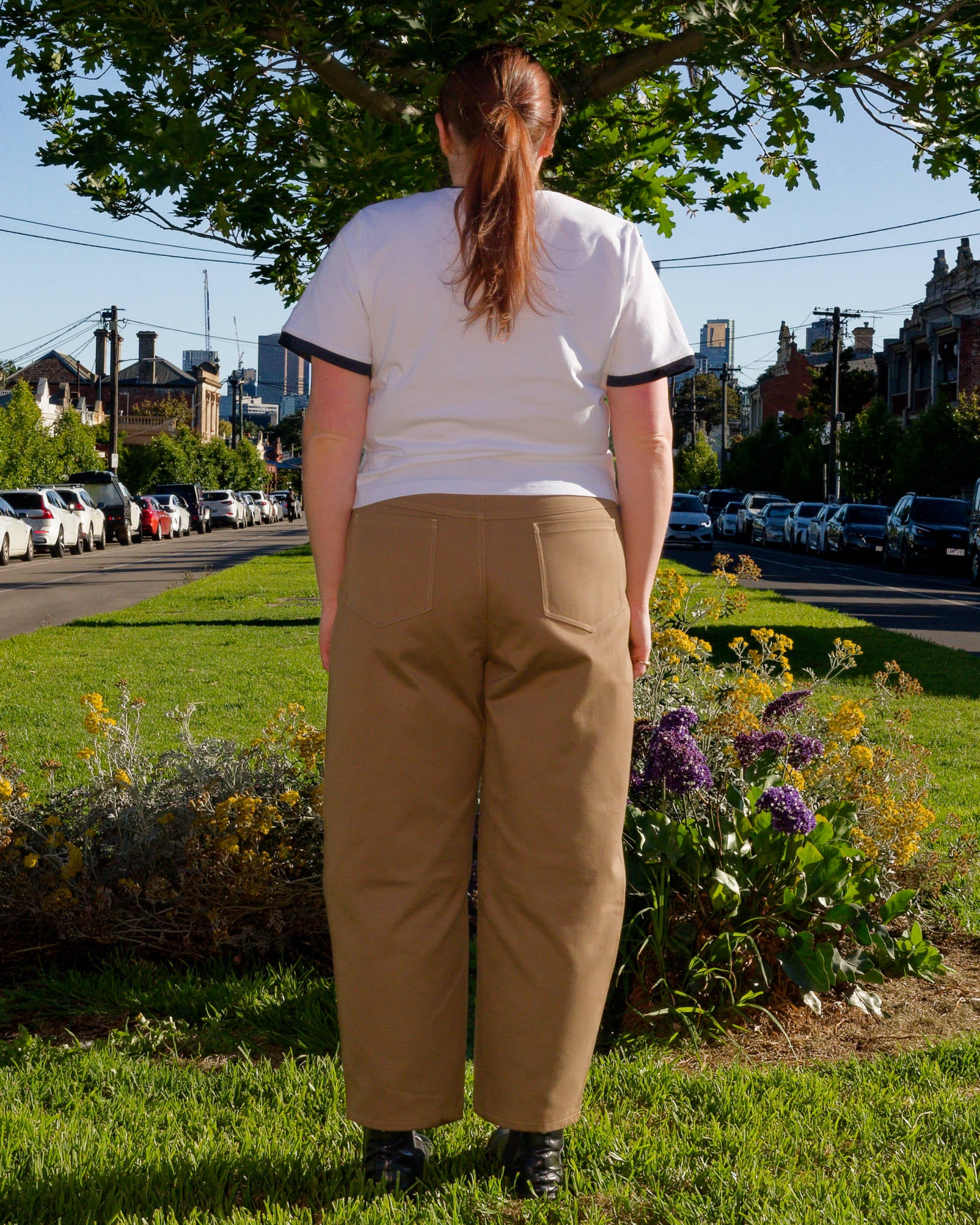 Lydia, facing backwards, modelling a white t-shirt and khaki barrel-leg jeans on a nature strip.