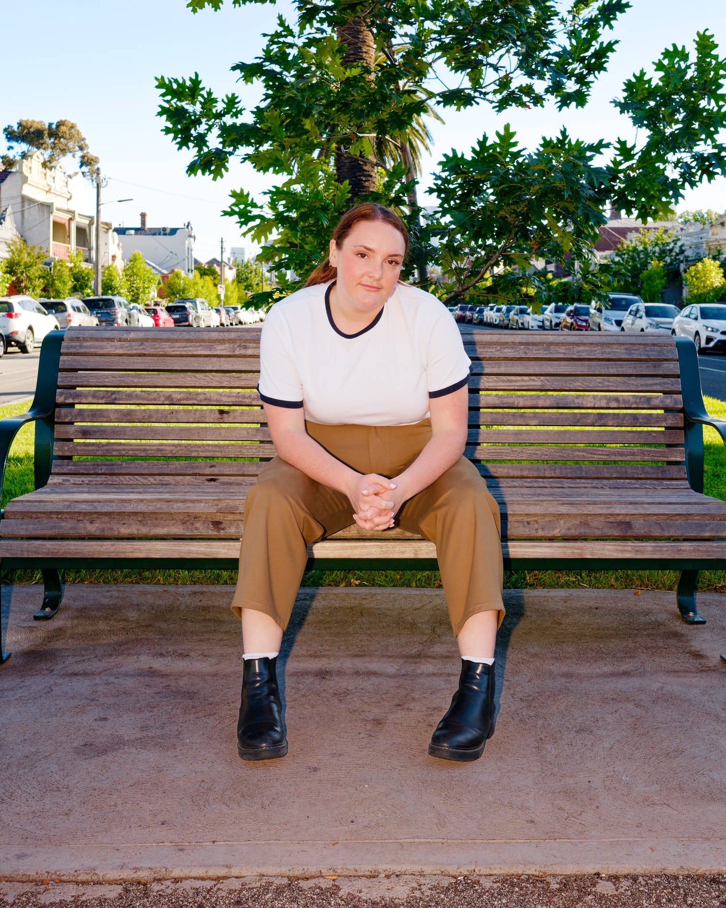 Lydia, sitting on a park bench, modelling a white t-shirt with navy trim and khaki barrel-leg jeans and black boots.