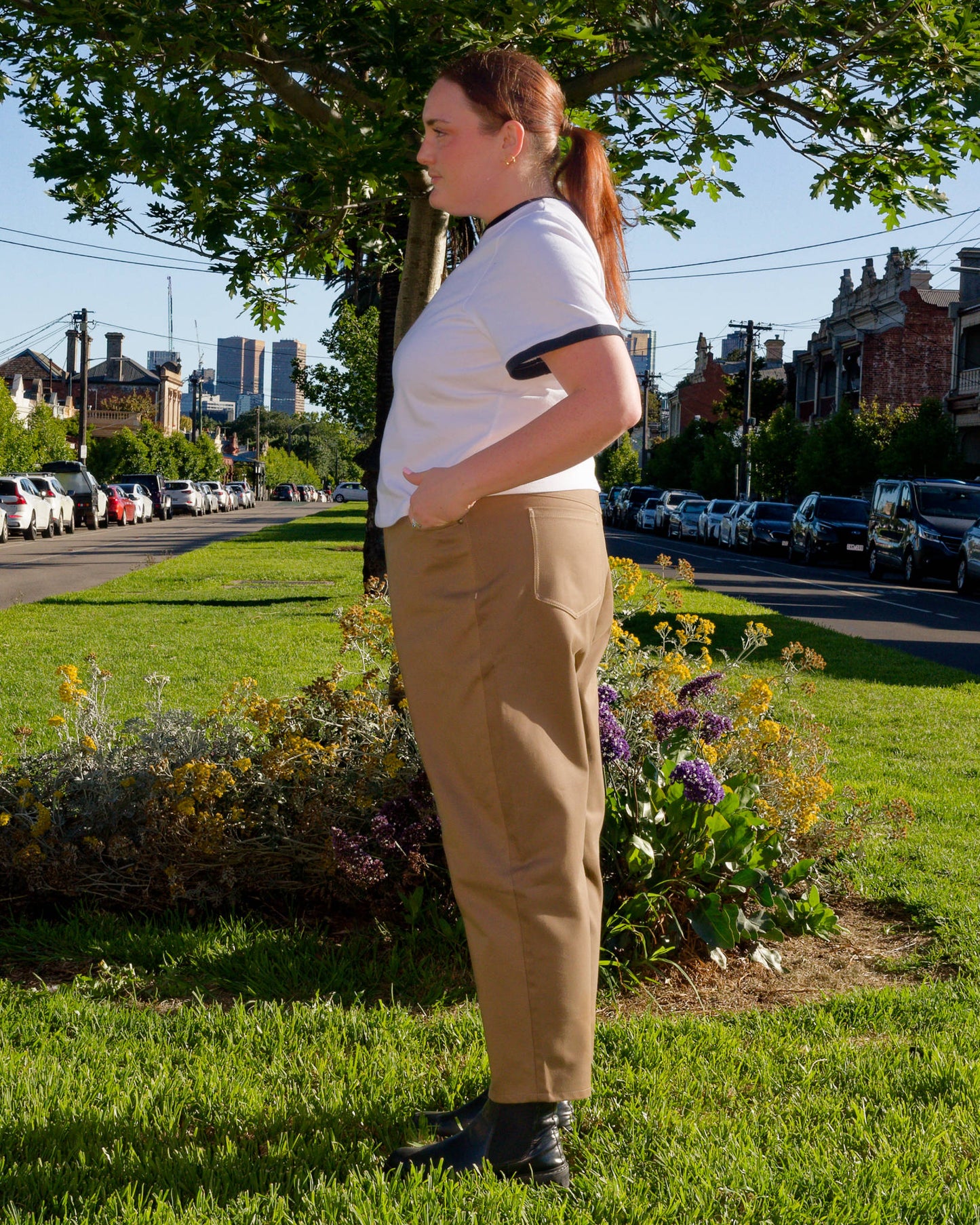 Lydia, facing side-on, modelling a white t-shirt and khaki barrel-leg jeans on a nature strip.