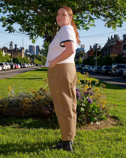 Lydia, facing side-on, modelling a white t-shirt and khaki barrel-leg jeans on a nature strip.