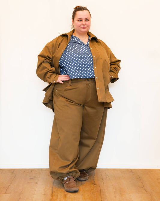 Hannah, in front of a white wall, modelling khaki wide-leg jeans and a khaki chore jacket over a a blue polkadot shirt.