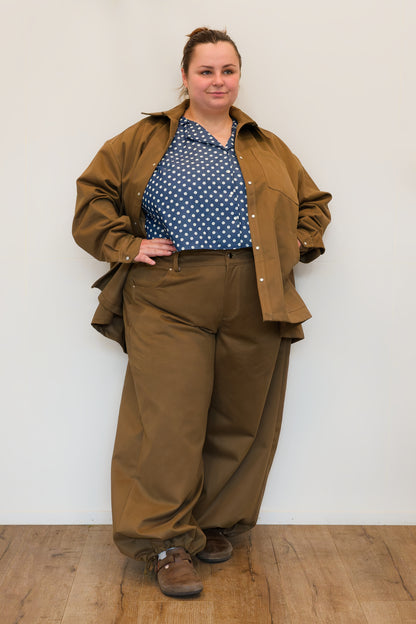 Hannah, in front of a white wall, modelling khaki wide-leg jeans and a khaki chore jacket over a a blue polkadot shirt.