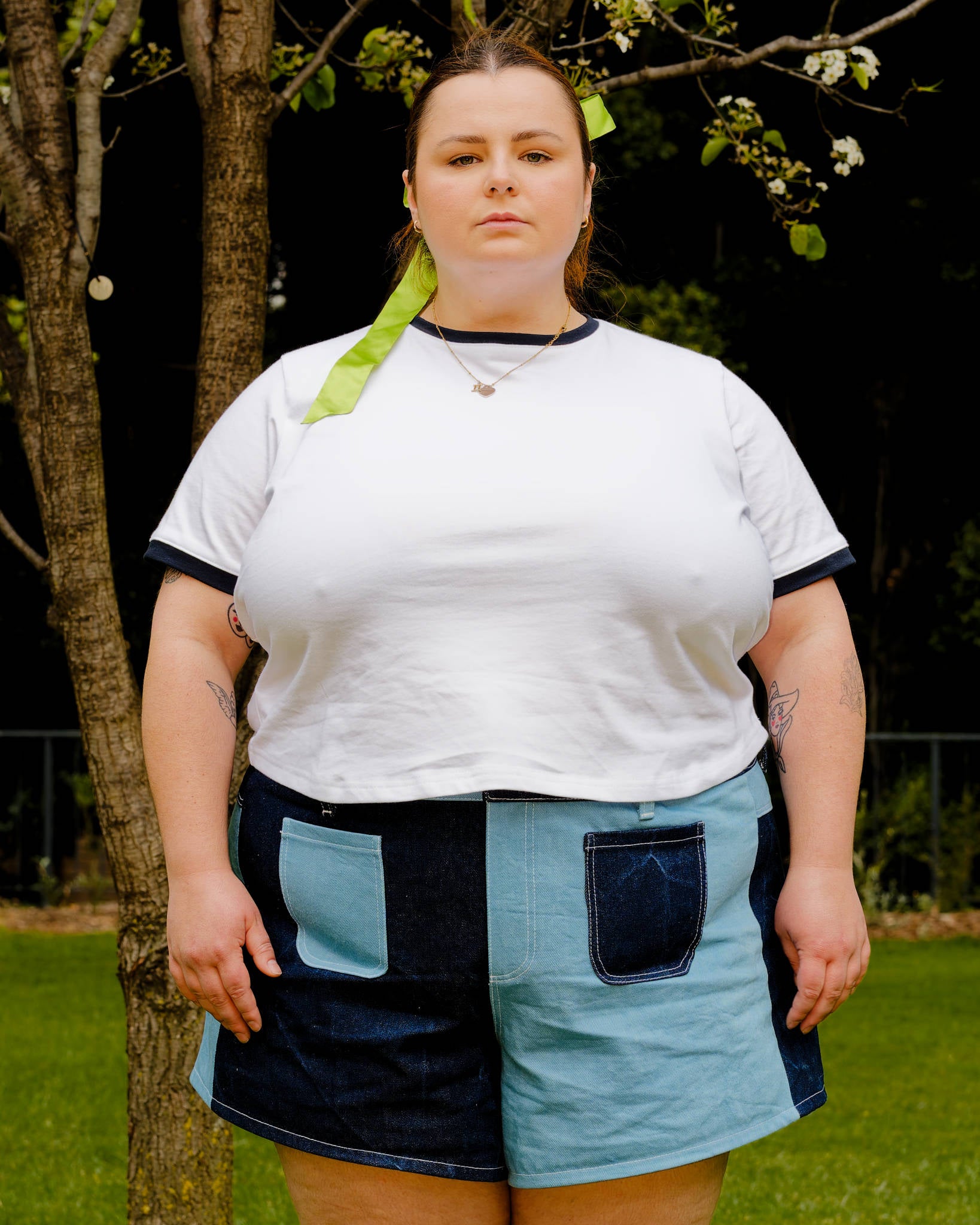 Hannah modelling a white t-shirt with navy trim and two-tone blue jean shorts in a park with trees.