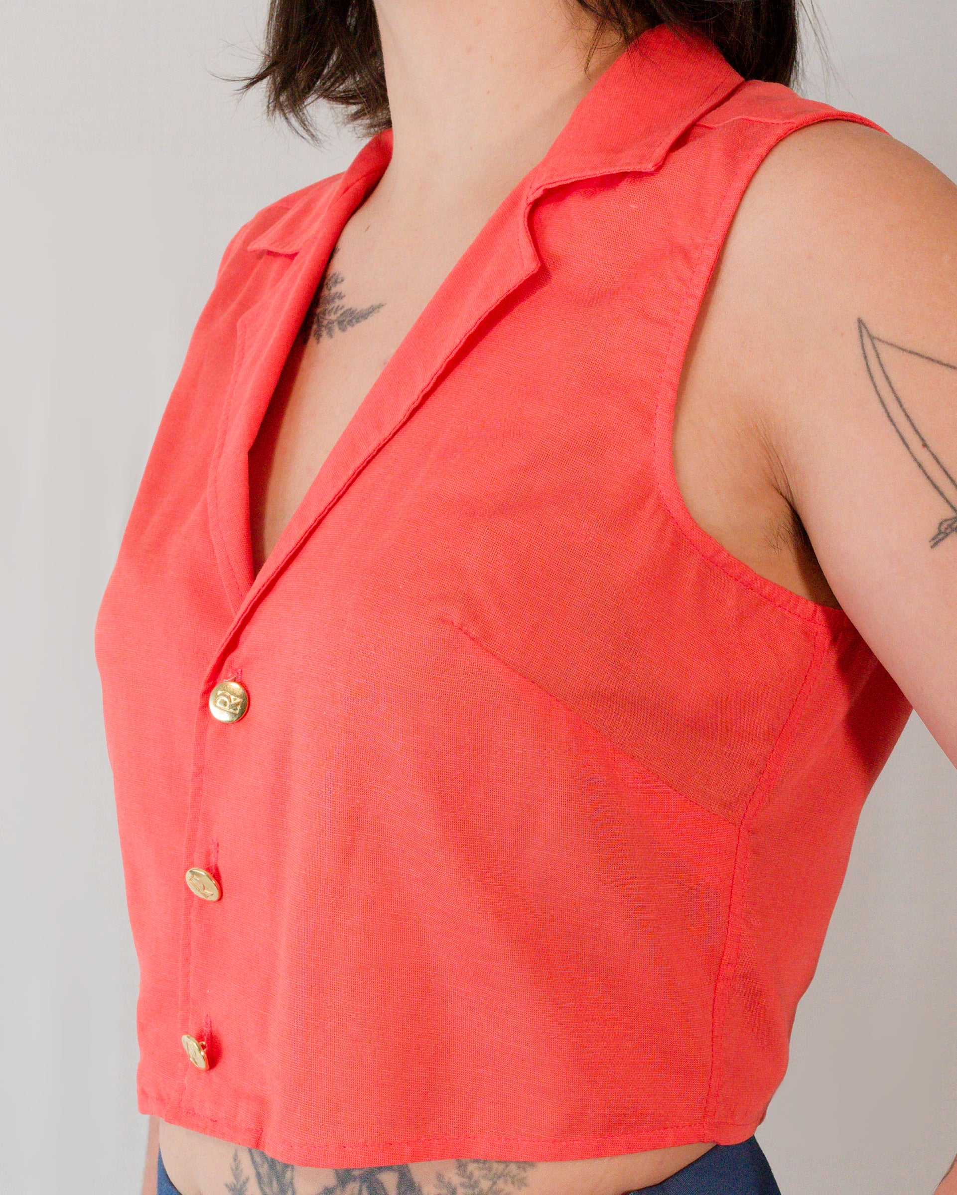 Close-up of sleeveless blouse in callistemon red showing bust darts, camp collar and brass buttons.