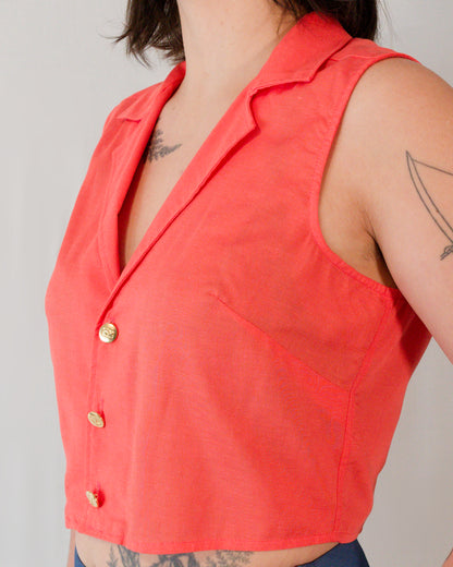 Close-up of sleeveless blouse in callistemon red showing bust darts, camp collar and brass buttons.