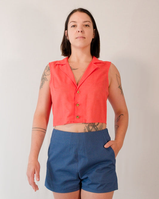 Front of sleeveless blouse in callistemon red with camp collar and brass buttons. Paired with Kingfisher A-line shorts in blue.