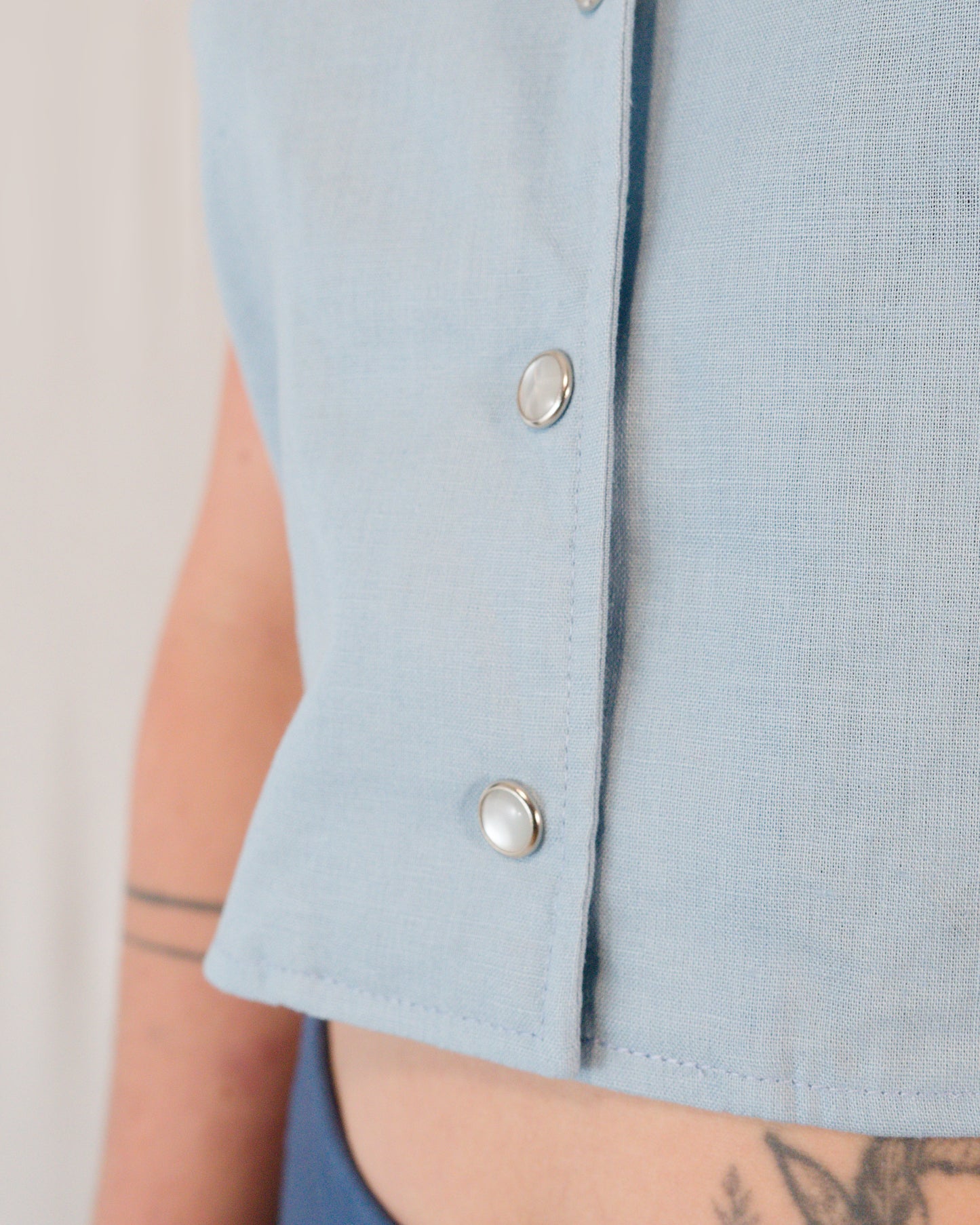 Close-up of pearl snaps on sleeveless blouse in skyline blue.