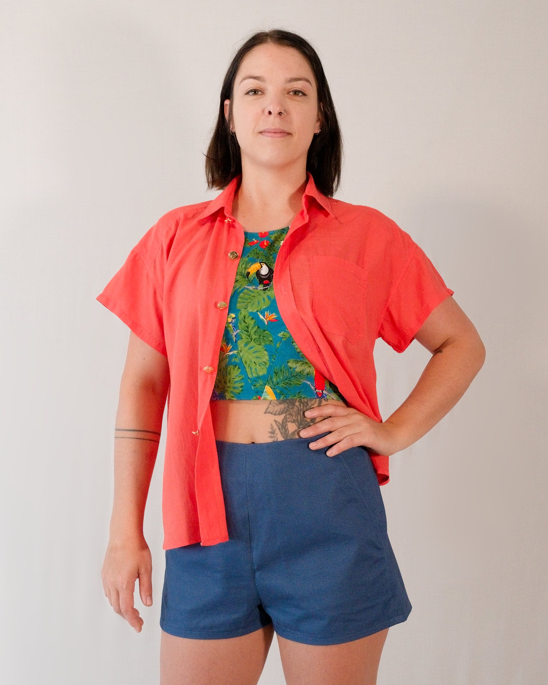 Short-sleeved blouse in callistemon red worn unbuttoned over a crop top in a turquoise parrot print.