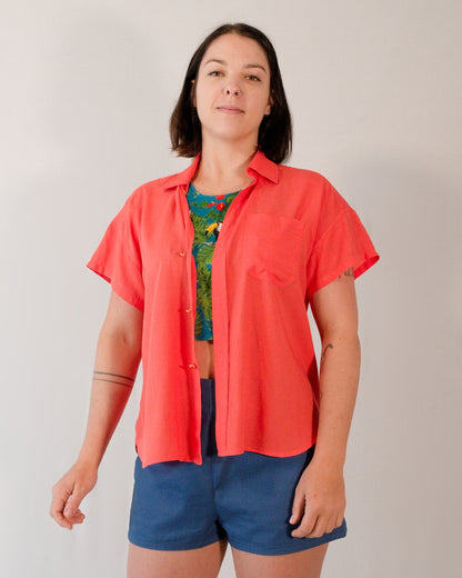 Short-sleeved blouse in callistemon red worn unbuttoned over a crop top in a turquoise parrot print.