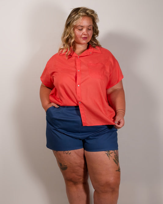 Front of a short-sleeved button-down blouse in callistemon red with one half of the blouse tucked in.