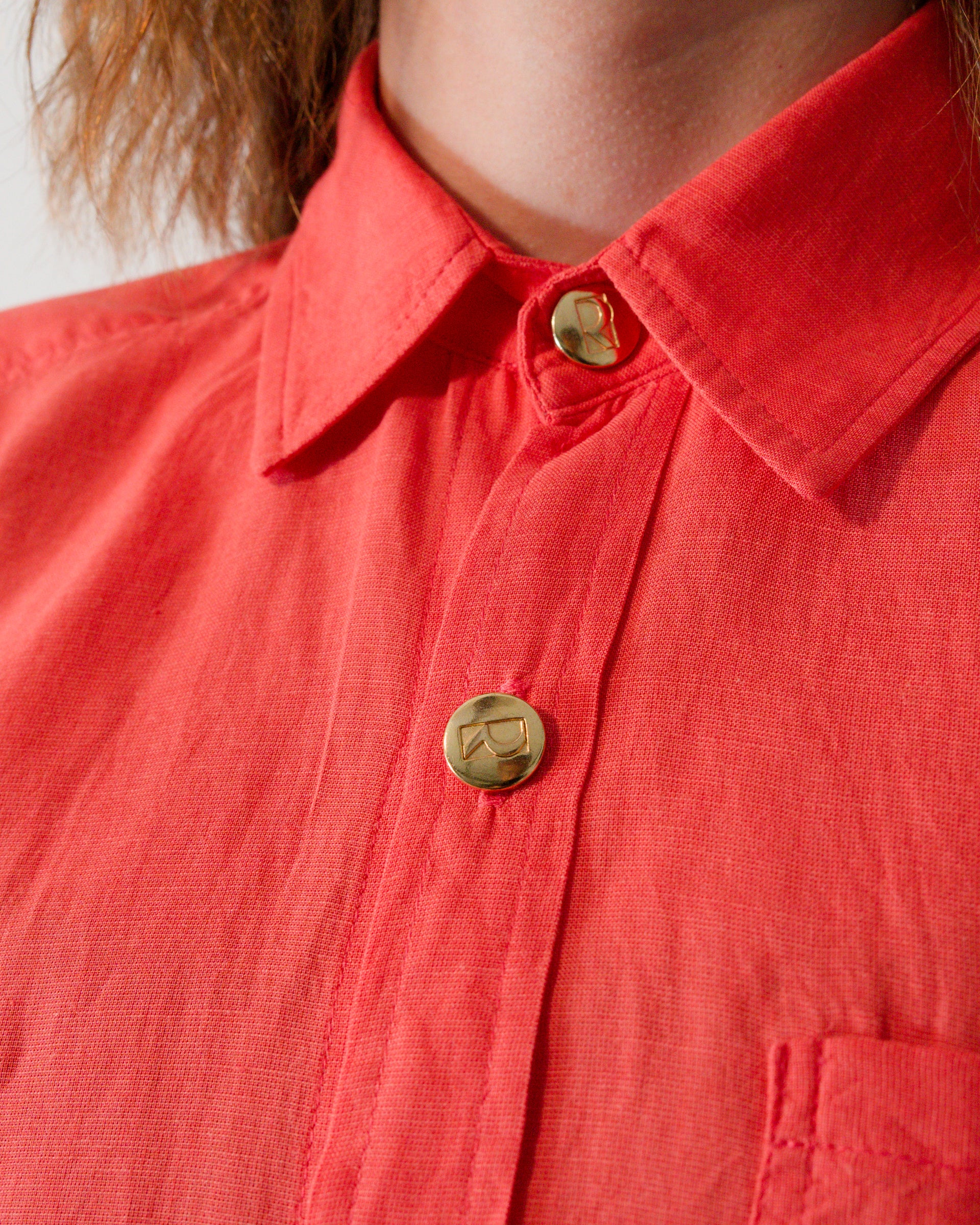 Close-up of collar and brass buttons on short-sleeved blouse in callistemon red.