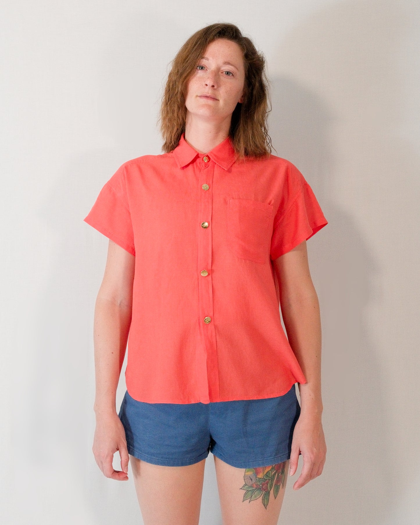 Front of a short-sleeved blouse in callistemon red with collar, brass buttons and left breast pocket.