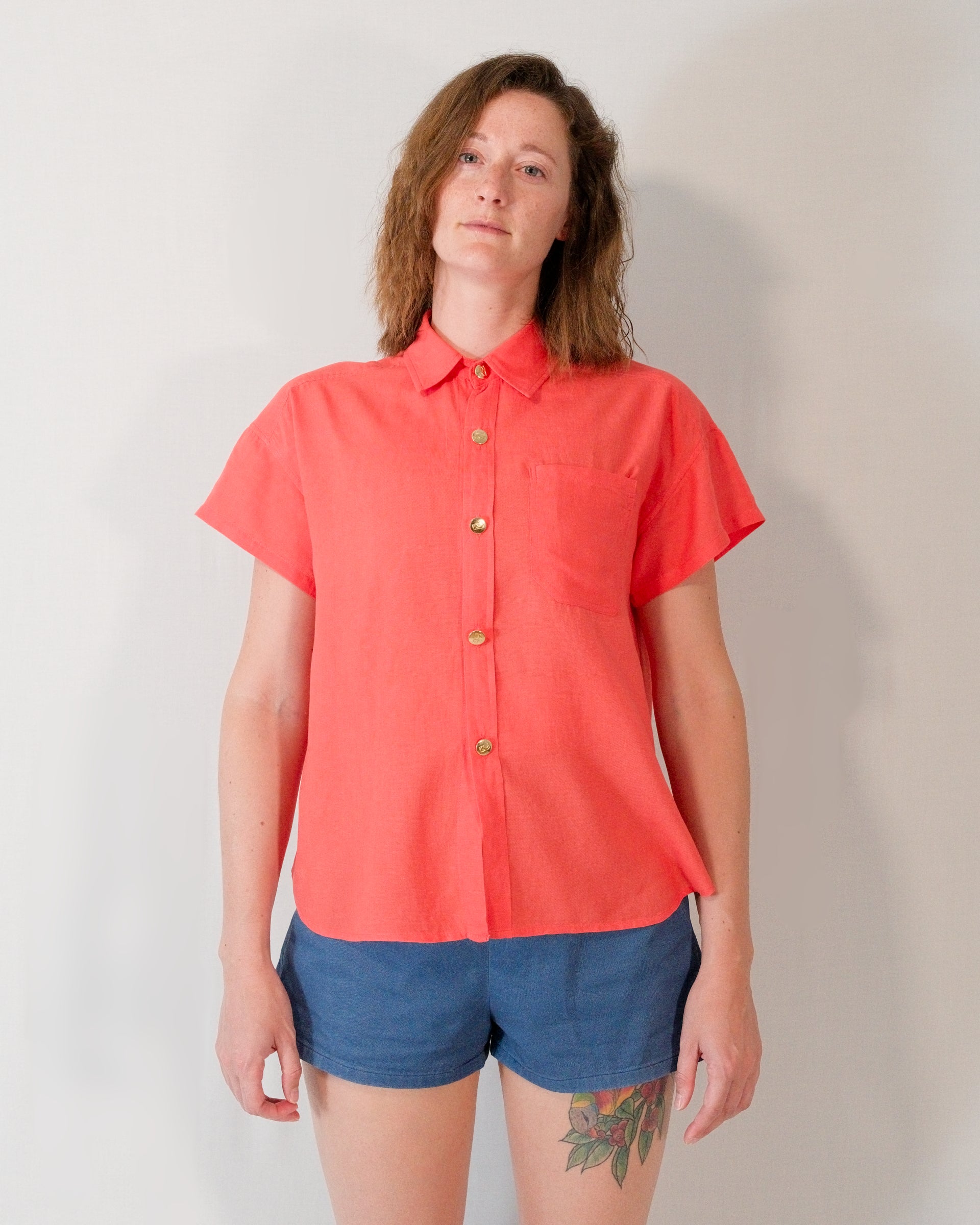 Front of a short-sleeved blouse in callistemon red with collar, brass buttons and left breast pocket.